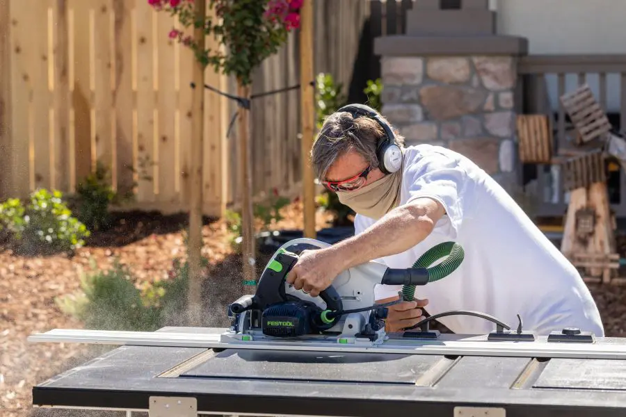 A man wearing headphones and working with a circular saw.